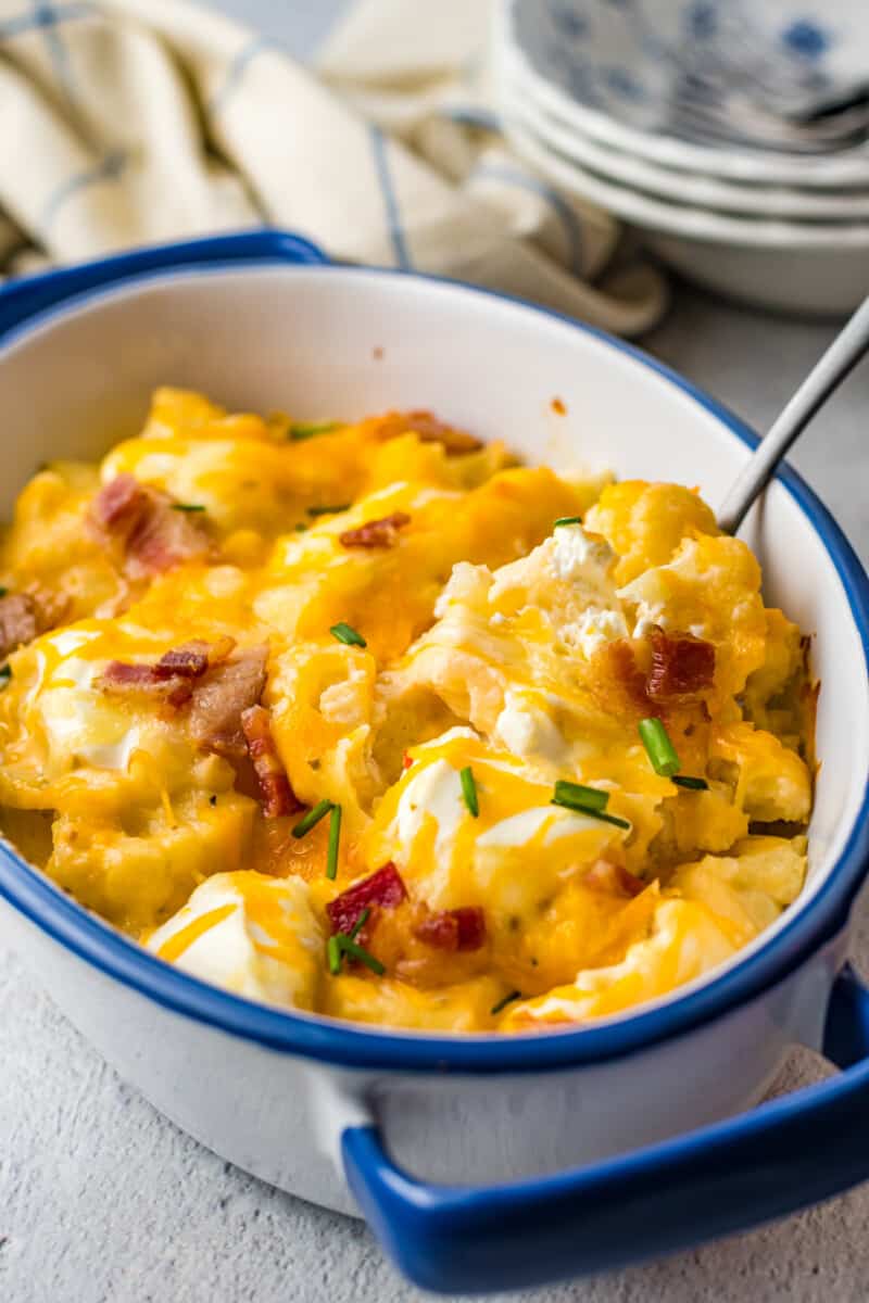 close up of loaded cauliflower bake in a blue and white casserole dish with a spoon.