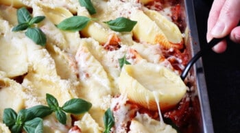 hand scooping a baked stuffed pasta shell out of baking pan