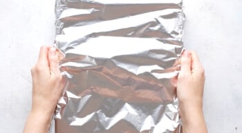 hands covering baking dish with aluminum foil