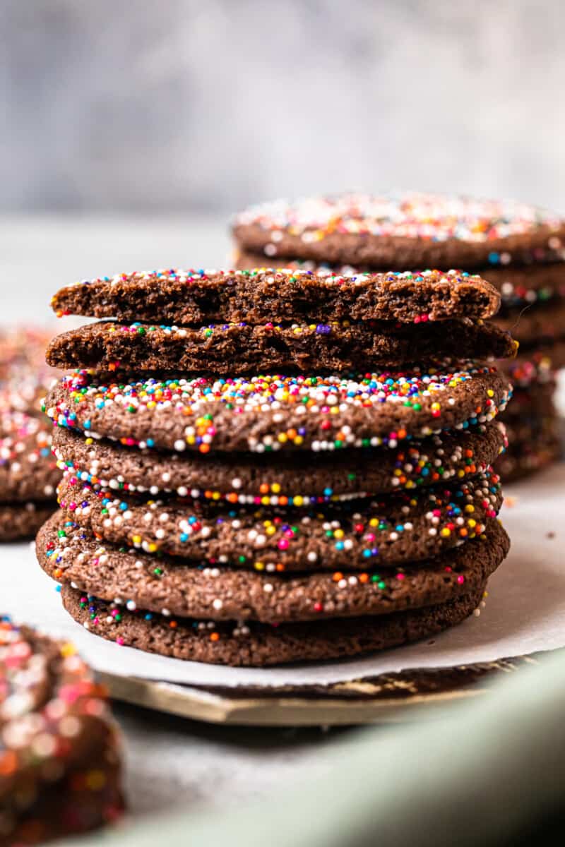 stack of 6 chocolate butter cookies on a white plate with the top cookie broken in half