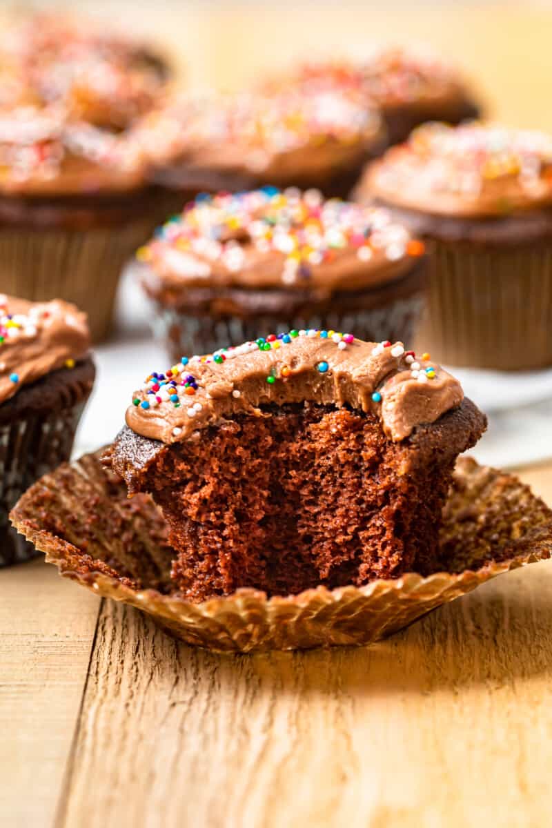 bite taken from a chocolate cupcake topped with chocolate frosting and sprinkles