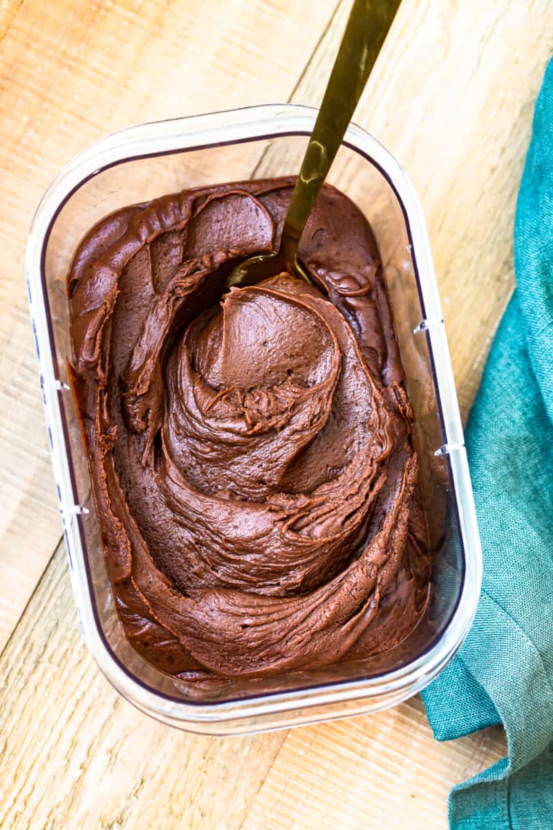 chocolate fudge frosting in a clear container with a serving spoon