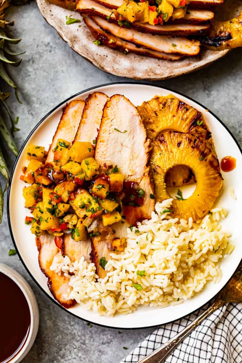 rice, grilled pineapple slices, and slices of huli huli turkey breast topped with pineapple salsa on a white plate