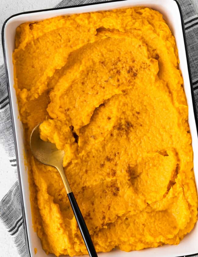 mashed sweet potatoes in a white rectangle baking dish with a serving spoon