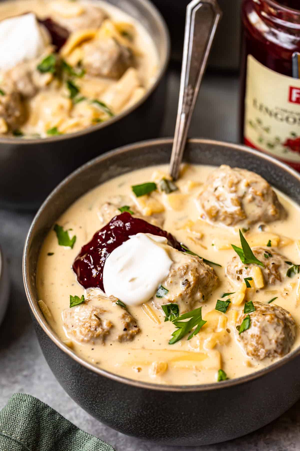 swedish meatball soup topped with sour cream and lingonberry jam in a bowl with a spoon.