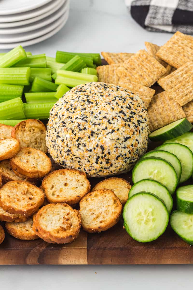 everything bagel cheeseball on a serving board with crackers, sliced cucumbers, and celery sticks ready for serving