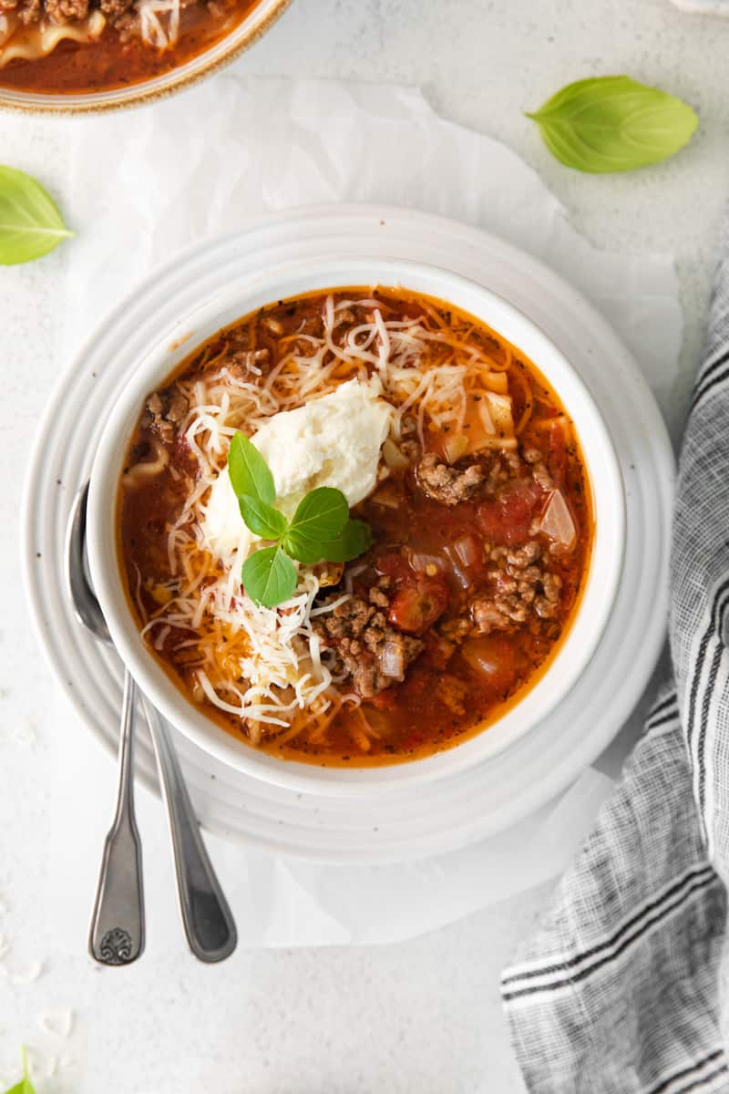 lasagna soup topped with ricotta cheese, parmesan cheese, and basil in a white bowl