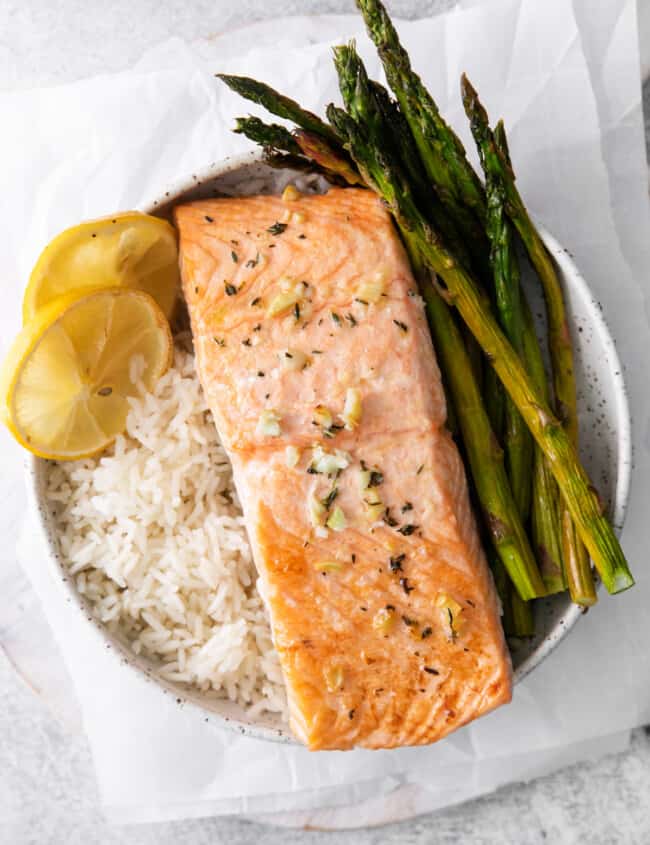 sheet pan lemon salmon on a bed of rice with asparagus in a white bowl.