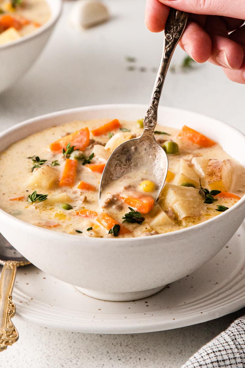 hand holding a spoon in a bowl of shepherd's pie soup