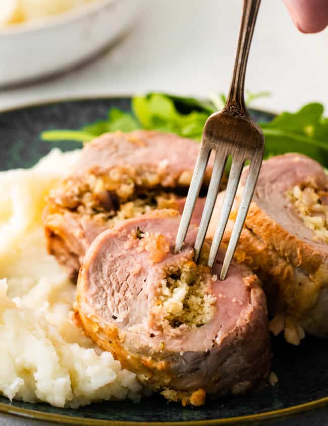 hand holding a fork in a piece of stuffed pork loin on a plate