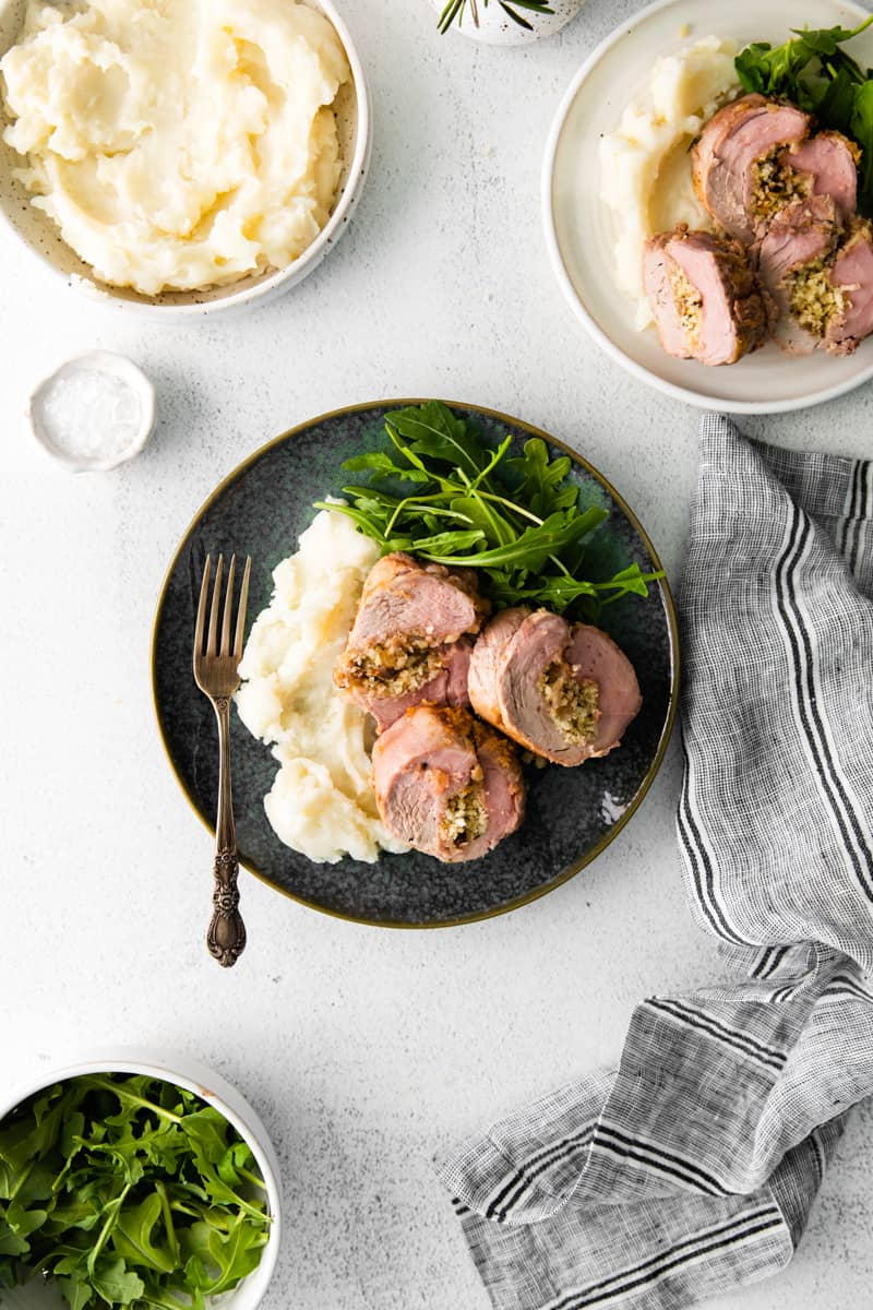 overhead image of dinner plates with mashed potatoes, slices of stuffed pork loin, and salad