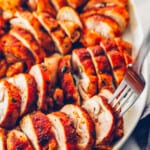 sliced baked chicken thighs on a white serving tray with a fork in one