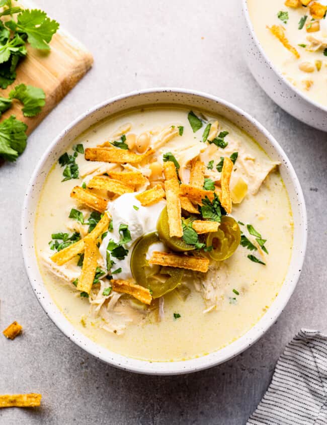 crockpot white chicken chili in white bowl garnished with cheese, jalapenos, and tortilla strips