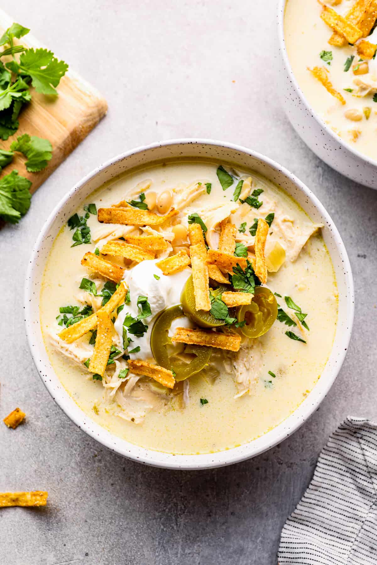 crockpot white chicken chili in white bowl garnished with cheese, jalapenos, and tortilla strips.