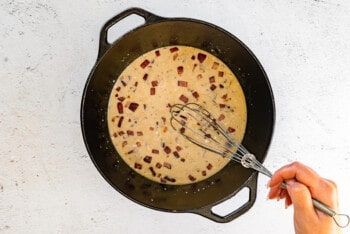 milk and flour mixture added to pot with onion and garlic with a whisk