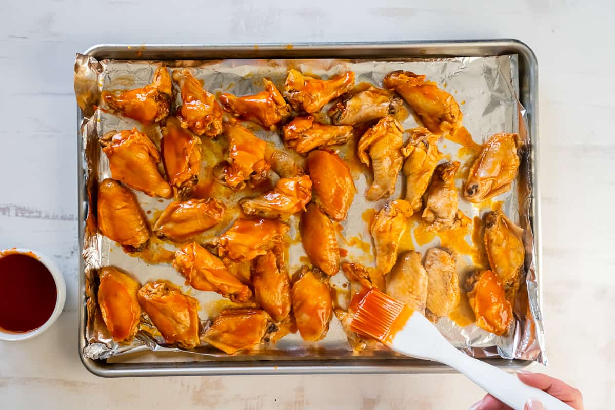 Brushing buffalo sauce onto a tray of cooked chicken wings.