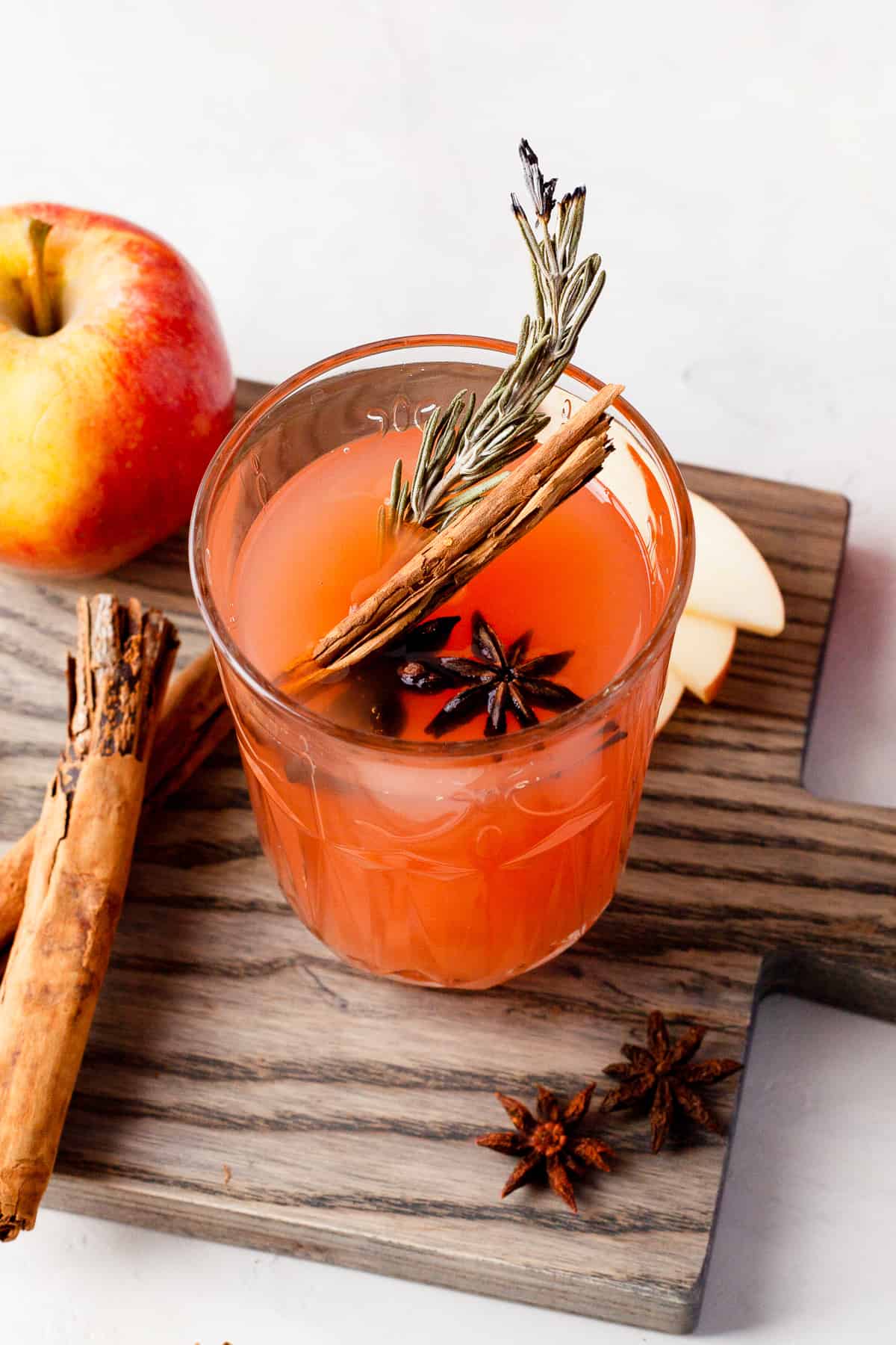 glass of instant pot apple cider garnished with cinnamon sticks and rosemary.