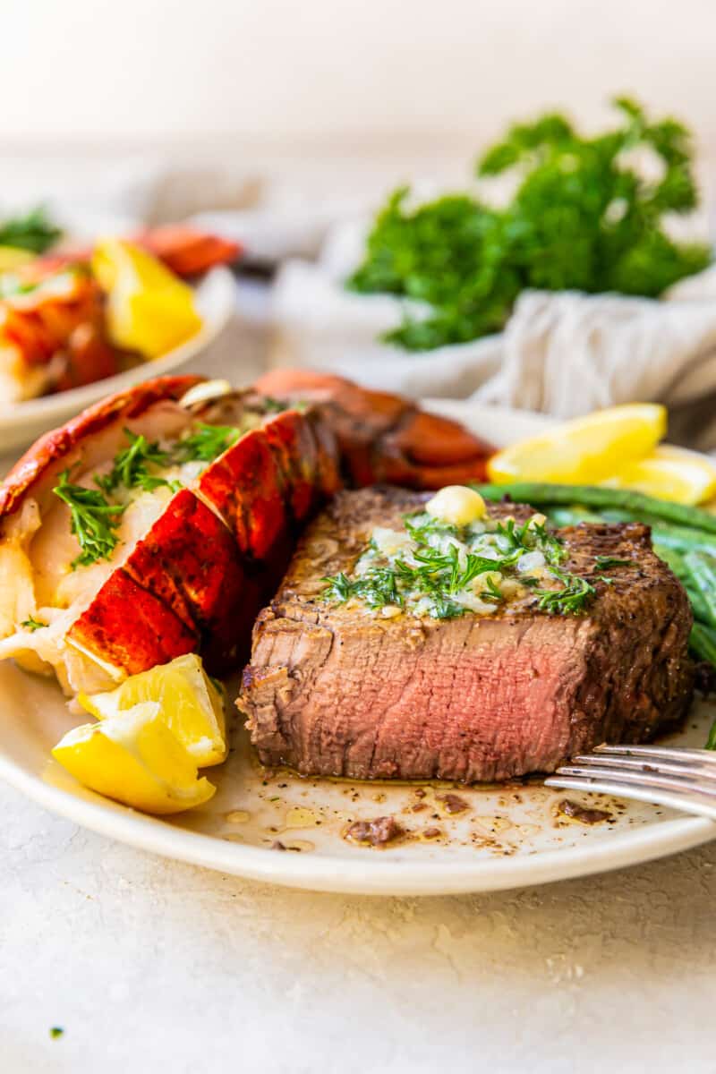 lobster tail and filet mignon with green beans on a plate with a fork