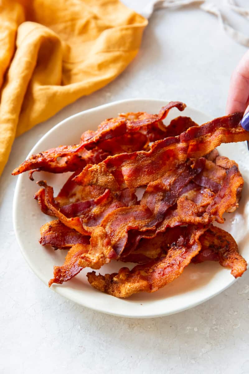 hand grabbing a slice of cooked bacon