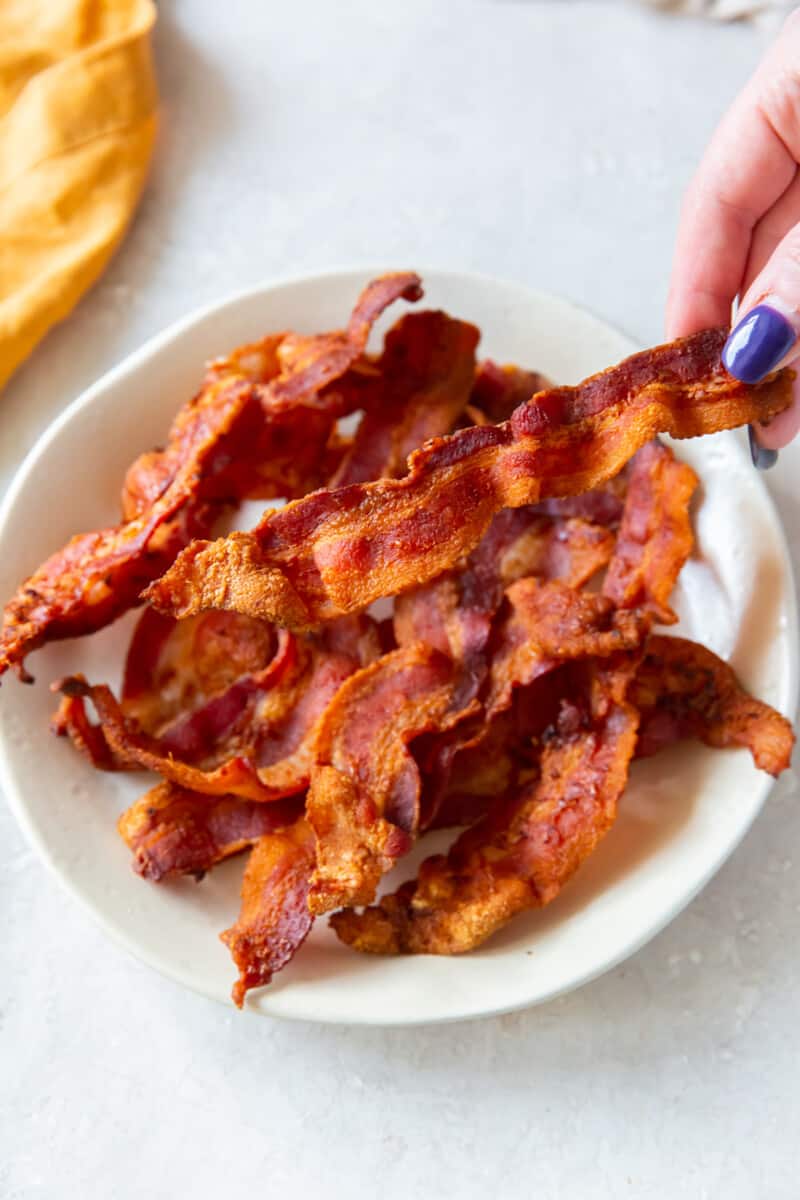 hand grabbing a piece of cooked bacon