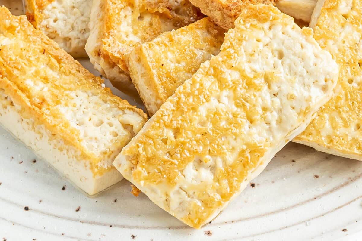 close up of pan fried tofu on a white plate.