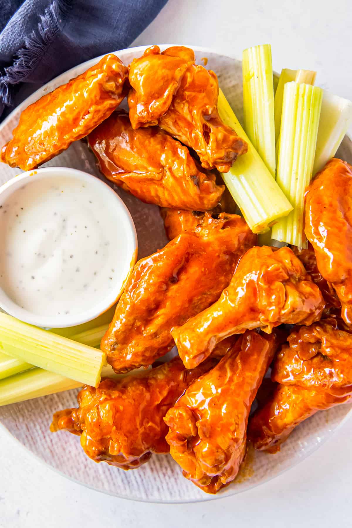 overhead image of buffalo chicken wings, sliced carrots, sliced celery, and dressing in a white bowl on a white plate