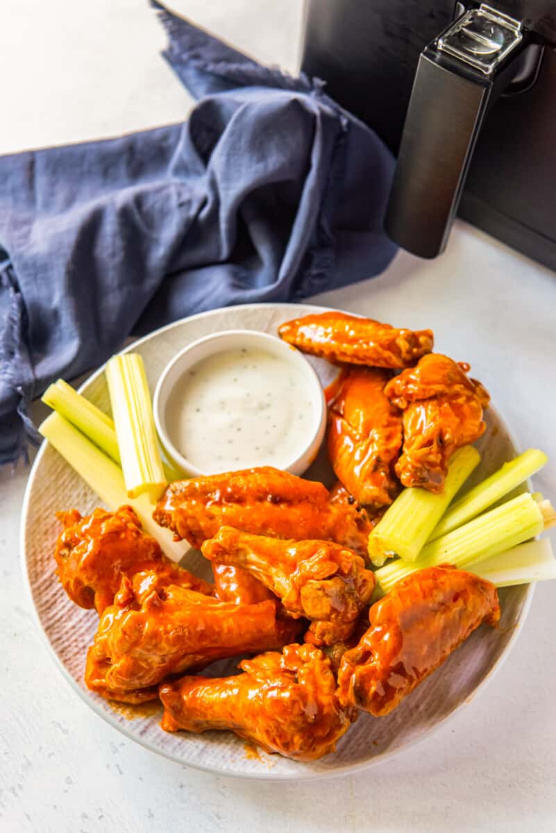 buffalo chicken wings, sliced carrots, sliced celery, and dressing in a white bowl on a white plate