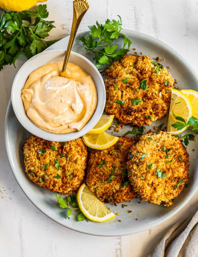 crab cakes on a plate with lemon slices and sauce in a bowl with a spoon