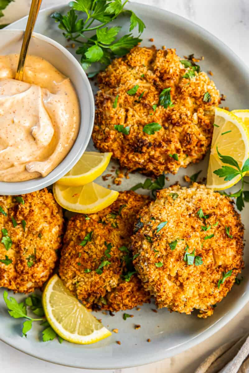 crab cakes on a plate with lemon slices and sauce in a bowl with a spoon