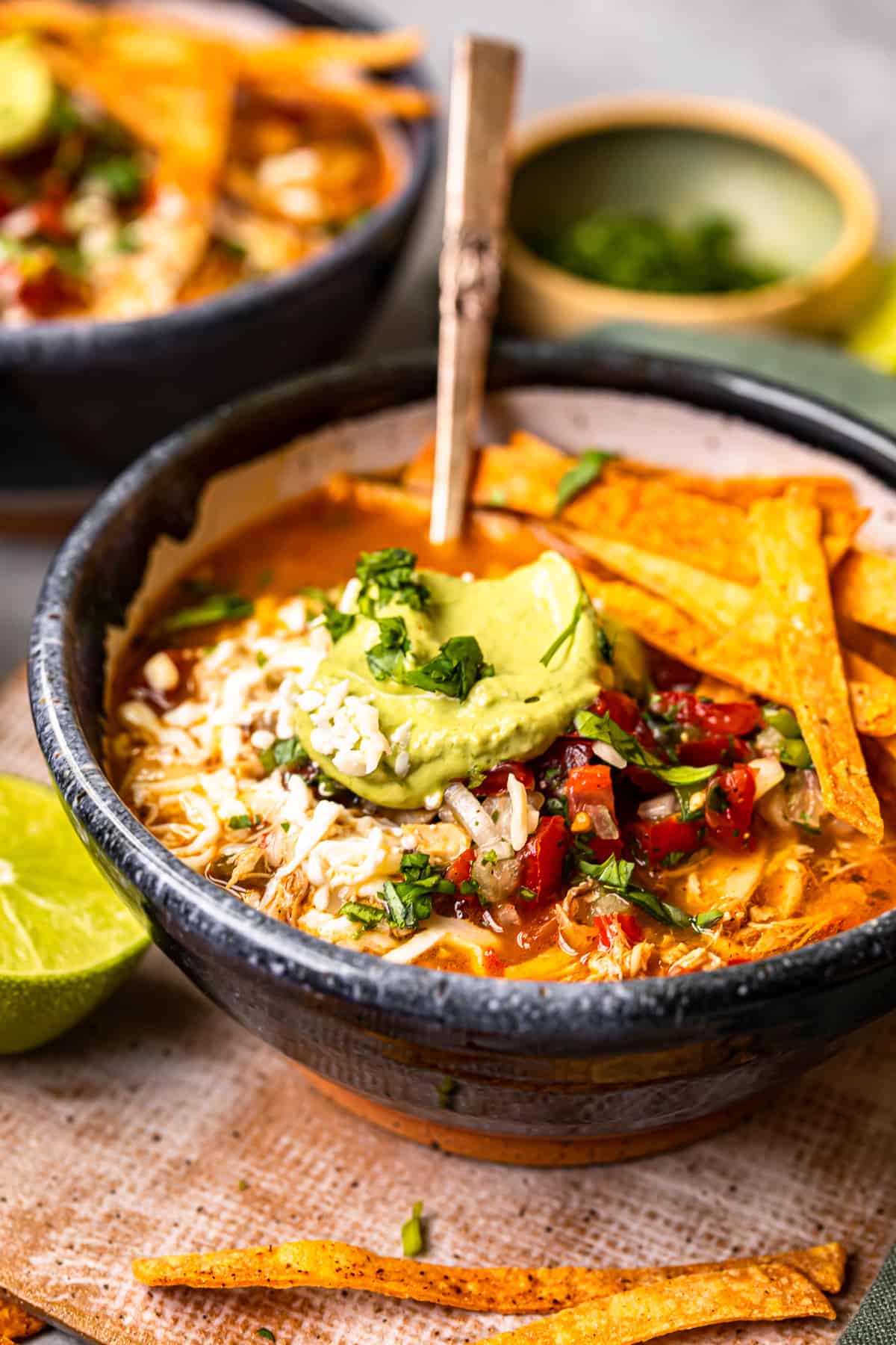 chicken fajita soup in a black bowl topped with cheese, guacamole, diced tomatoes, and tortilla strips with a spoon