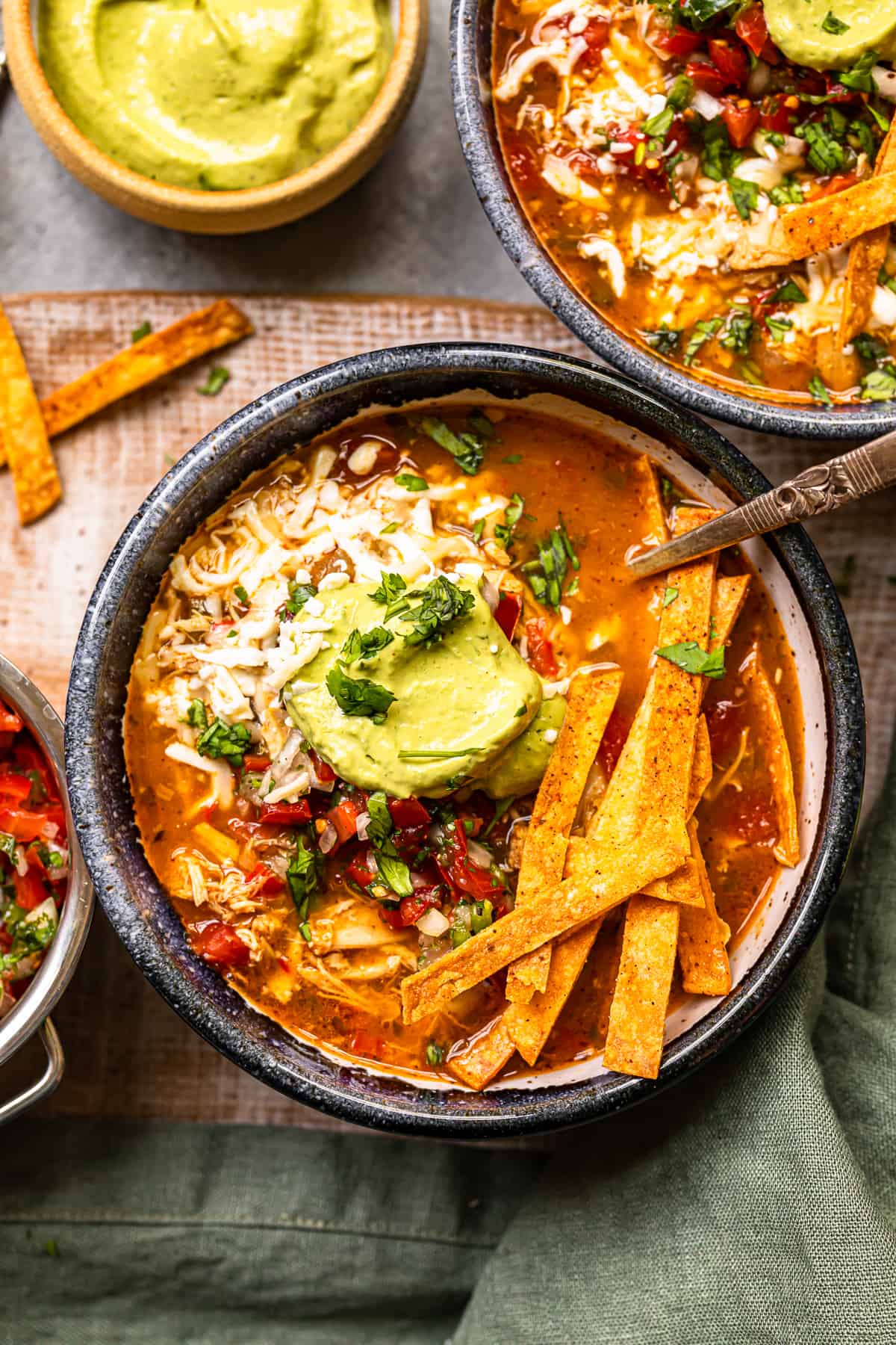 chicken fajita soup in a black bowl topped with cheese, guacamole, diced tomatoes, and tortilla strips with a spoon