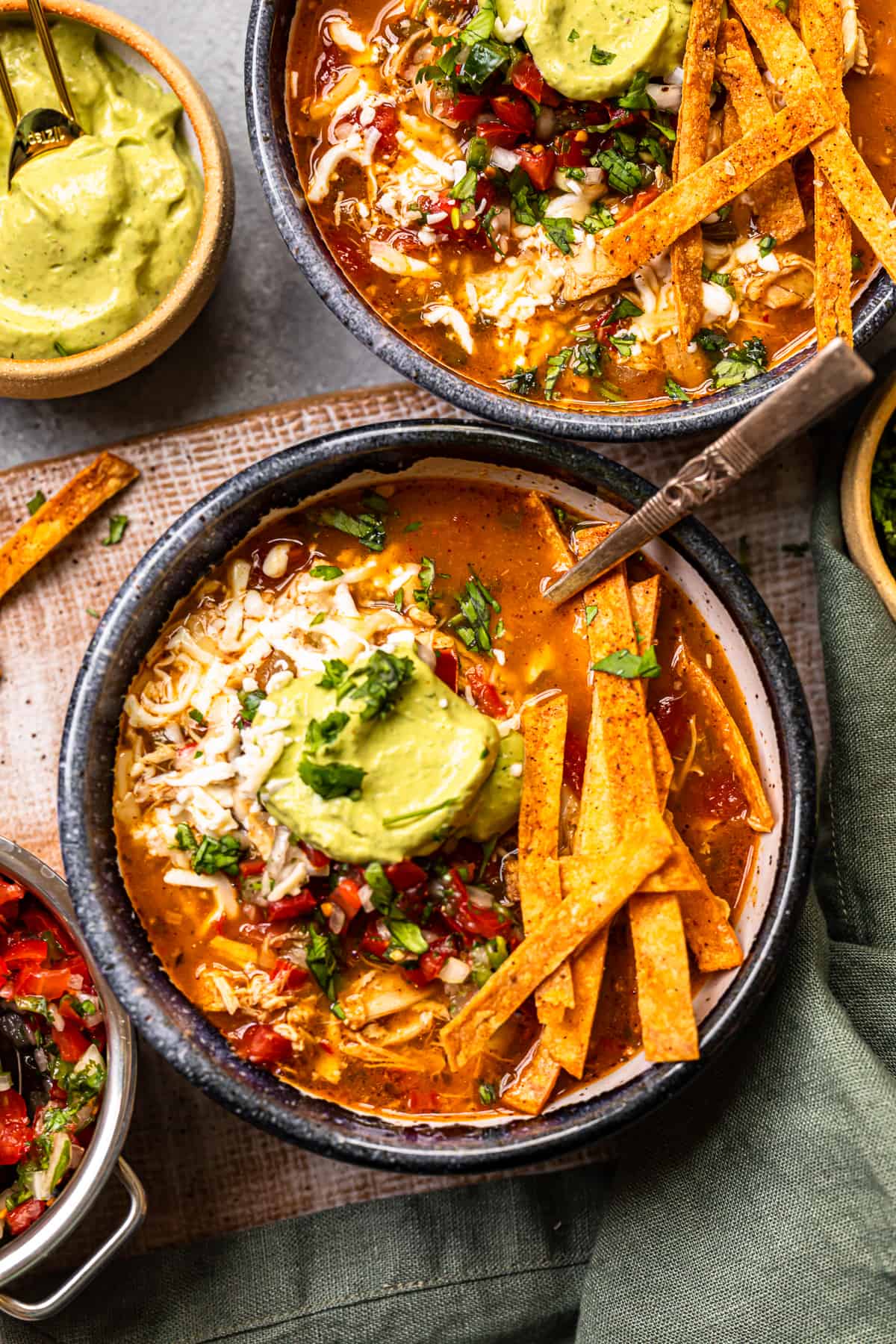 chicken fajita soup in a black bowl topped with cheese, guacamole, diced tomatoes, and tortilla strips with a spoon