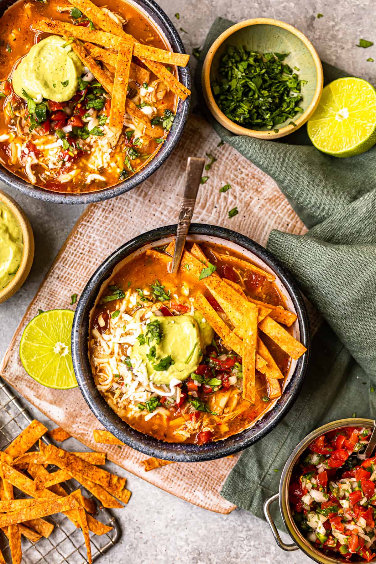 overhead image of chicken fajita soup in a black bowl topped with cheese, guacamole, diced tomatoes, and tortilla strips with a spoon