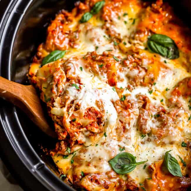 overhead view of a wooden spoon lifting a slice of lasagna from a crockpot.