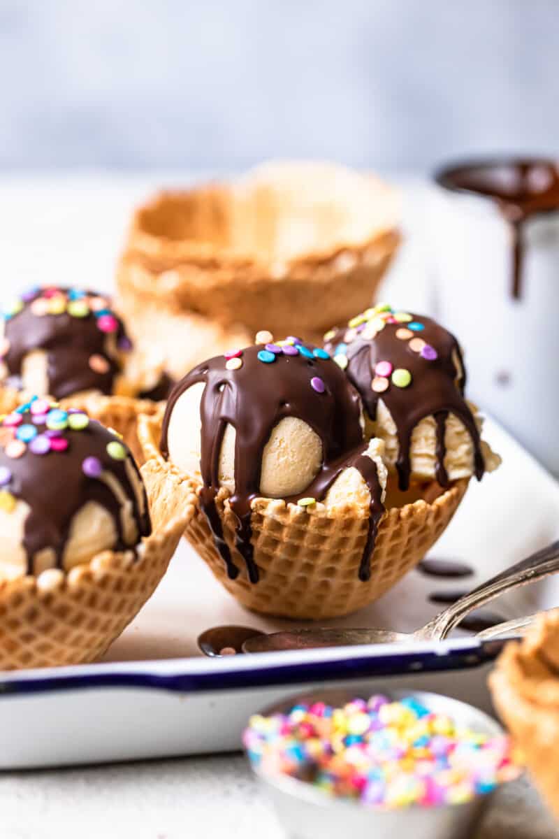 scoops of ice cream in waffle cone bowls topped with chocolate magic shell and sprinkles