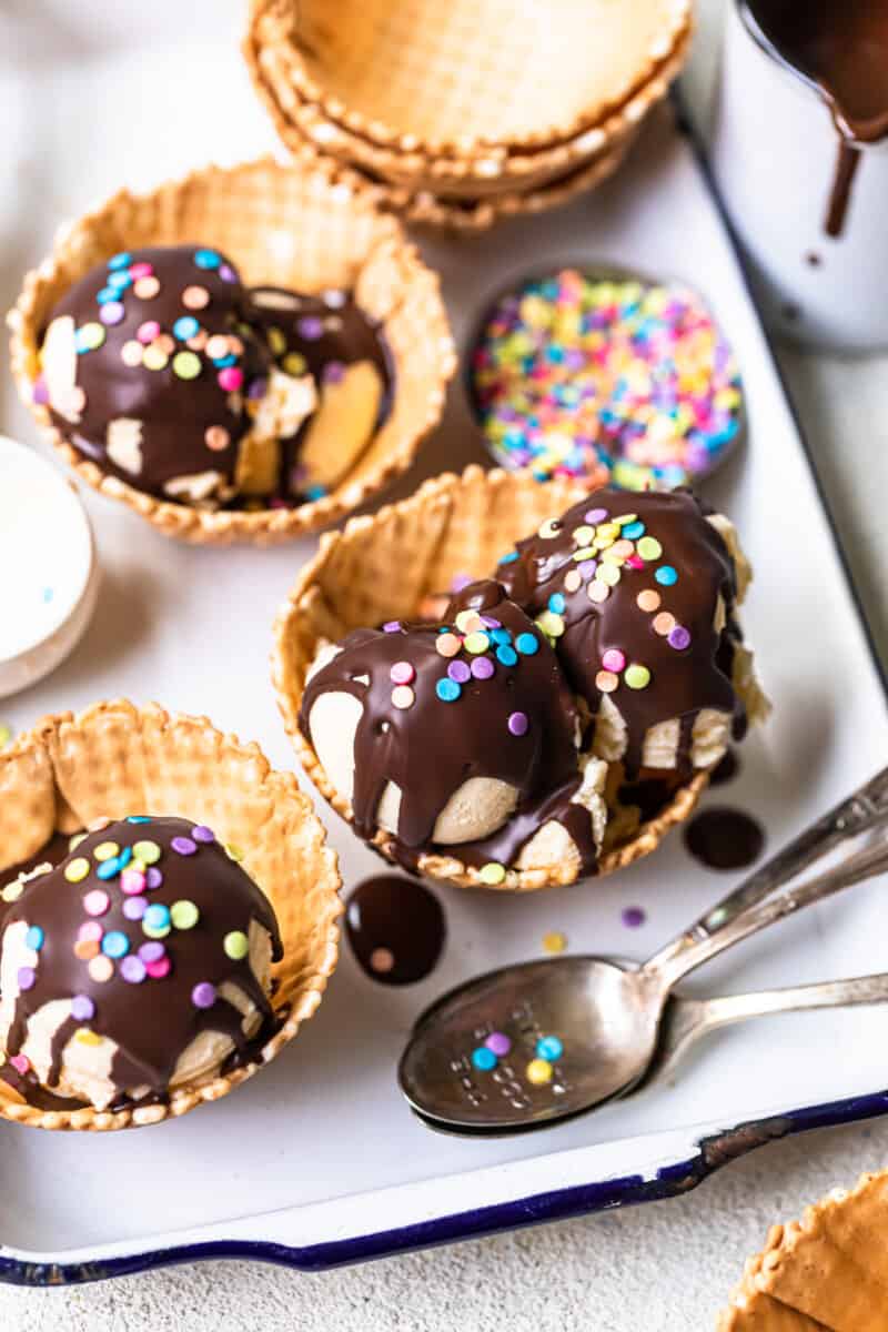 overhead image of scoops of ice cream in waffle cone bowls topped with chocolate magic shell and sprinkles