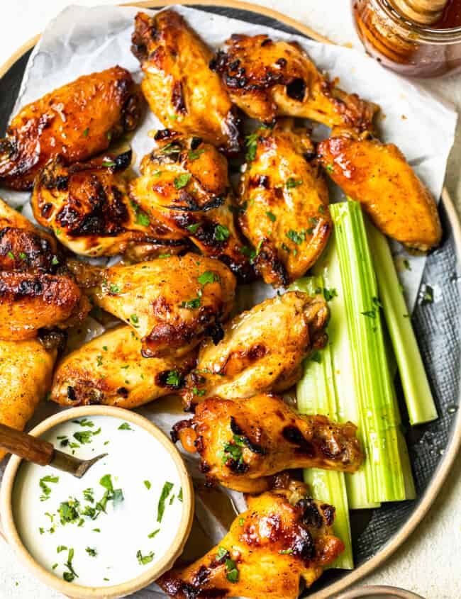 overhead image of hot honey chicken wings and celery slices on a serving tray with ranch dip in a small bowl with a spoon