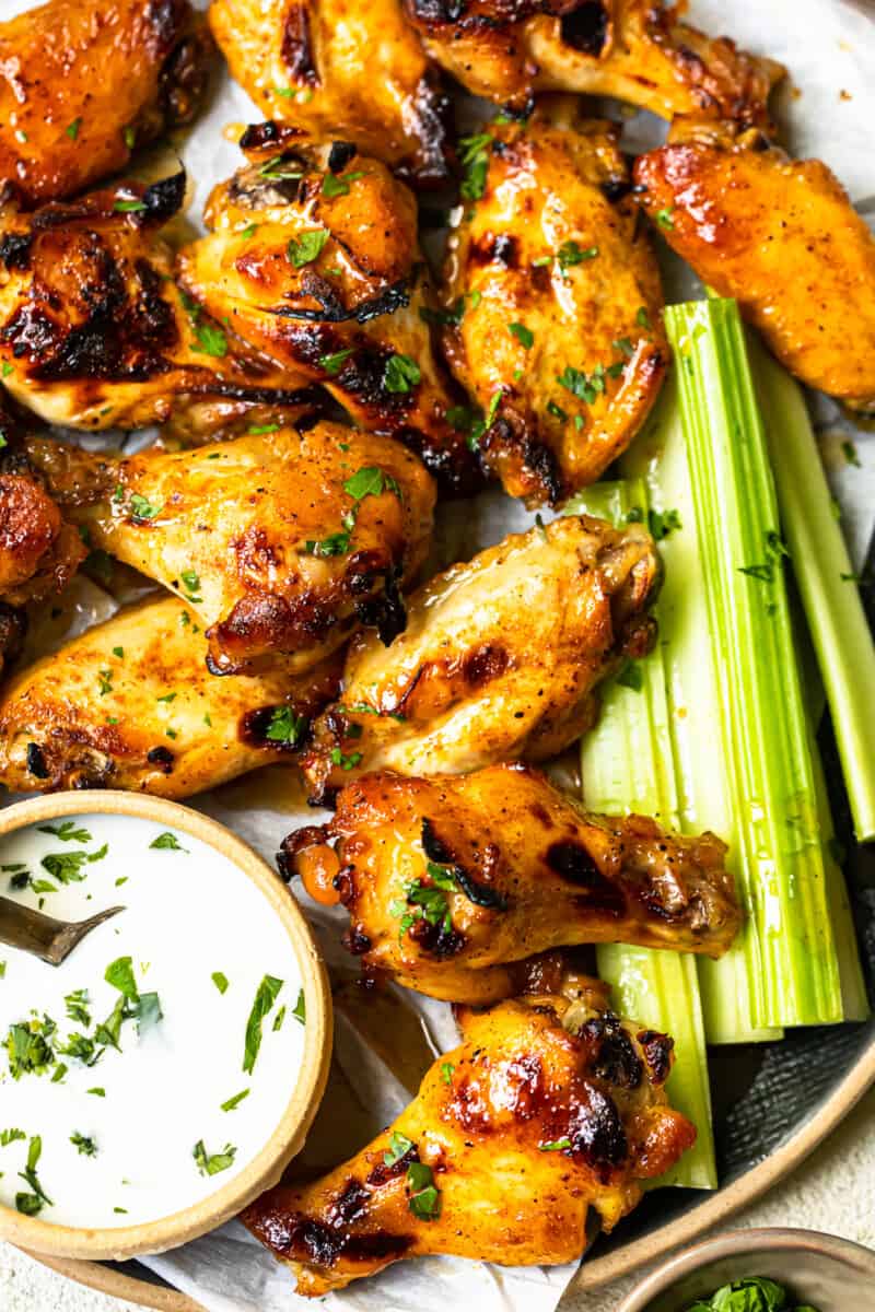 overhead image of hot honey chicken wings and celery slices on a serving tray with ranch dip in a small bowl with a spoon