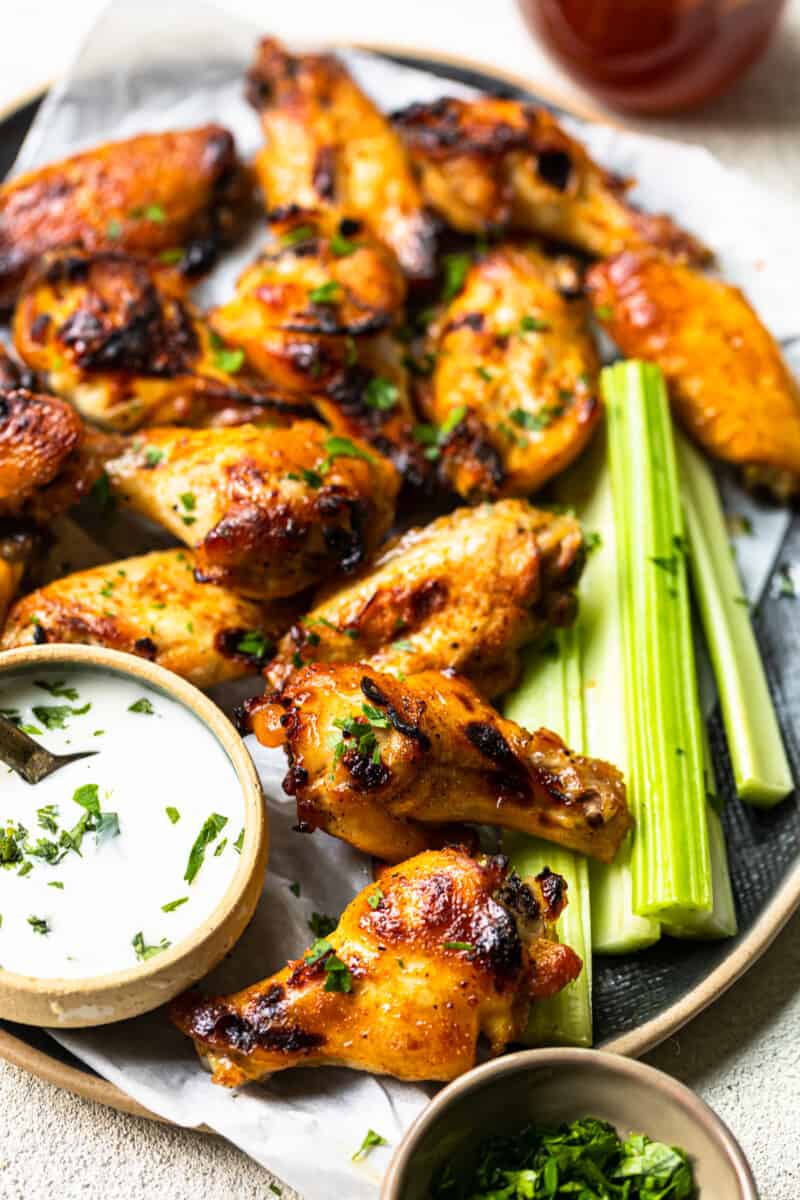 hot honey chicken wings and celery slices on a serving tray with ranch dip in a small bowl with a spoon