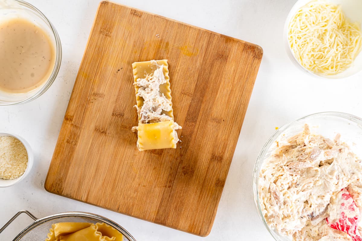 halfway rolled up lasagna noodle with chicken alfredo filling on a wood cutting board