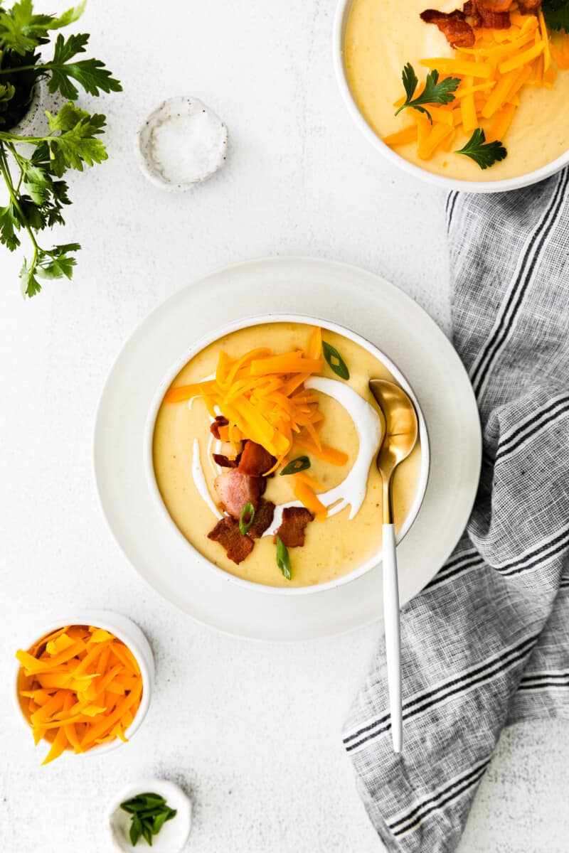 overhead image of creamy potato soup in a white bowl topped with shredded cheddar cheese and bacon with a spoon