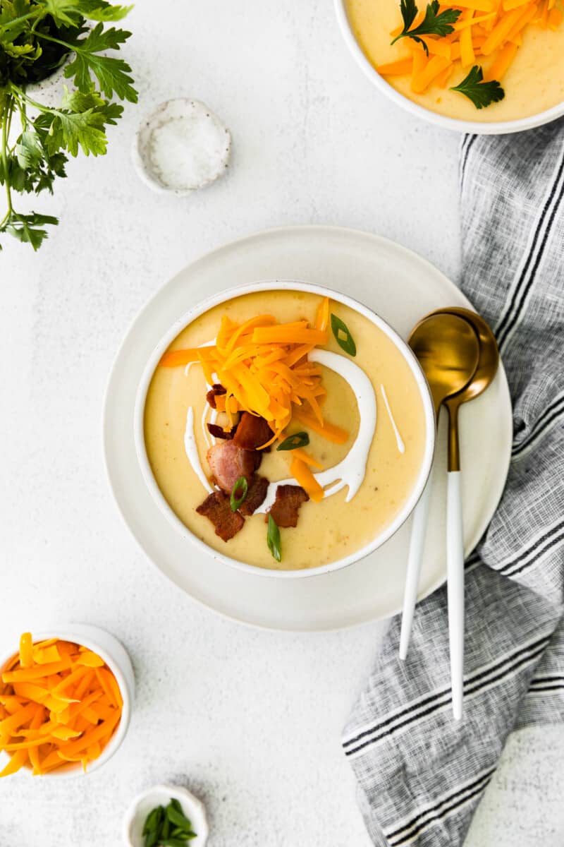 overhead image of creamy potato soup in a white bowl topped with shredded cheddar cheese and bacon with a spoon