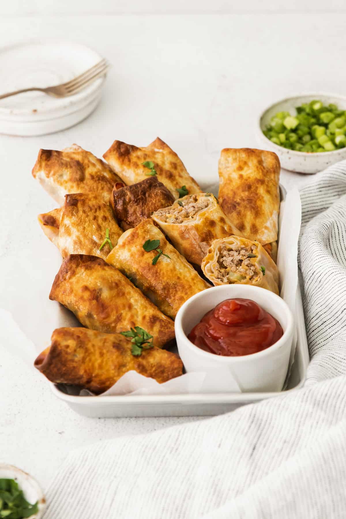 cheeseburger egg rolls on a serving tray with a side of ketchup in a white bowl.