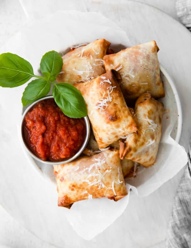 overhead image of pizza rolls in a white bowl with pizza sauce in a metal bowl