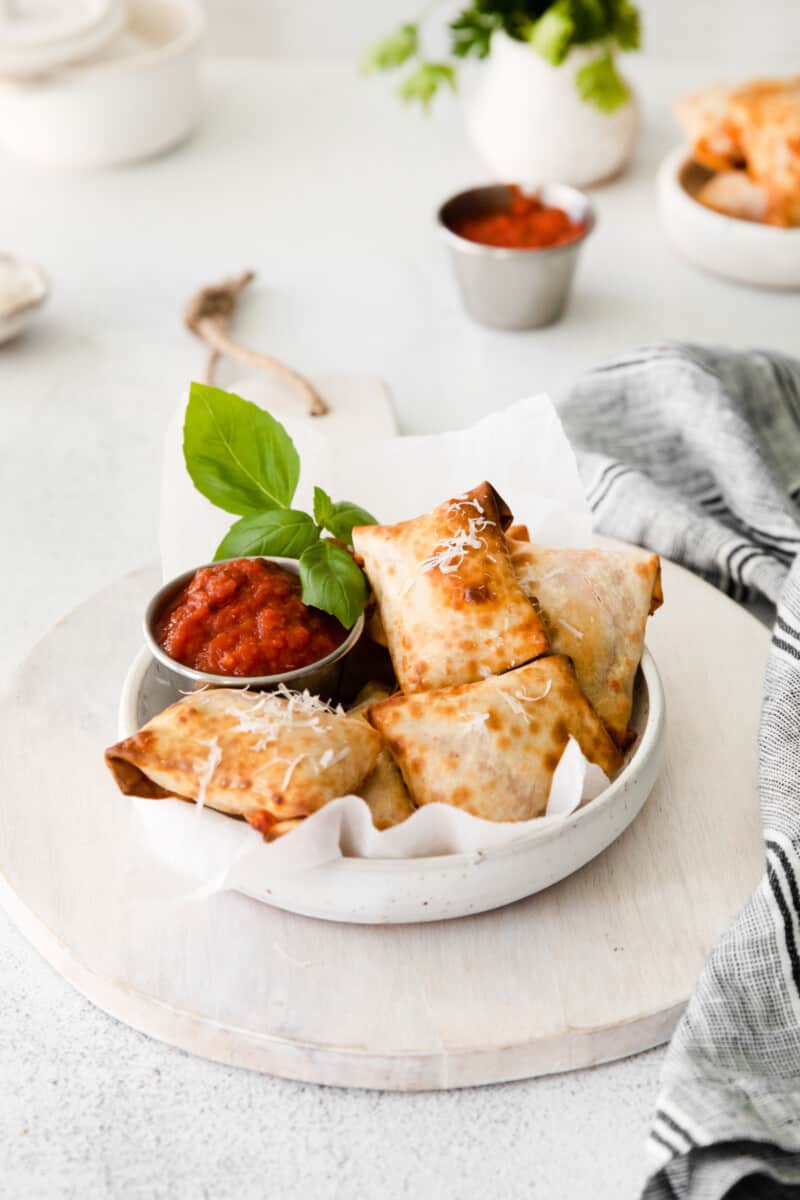 pizza rolls in a white bowl with pizza sauce in a metal bowl