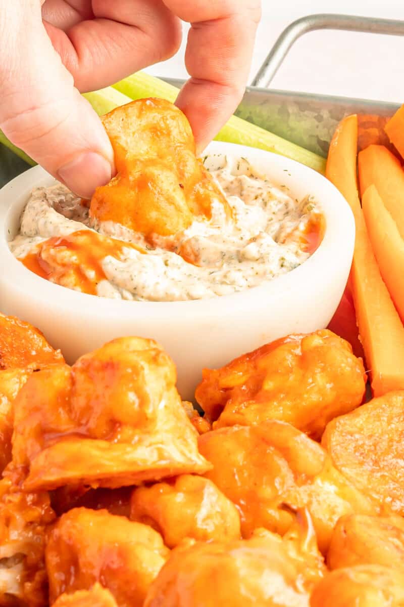 hand dipping a buffalo cauliflower wing into a bowl of buffalo ranch dressing