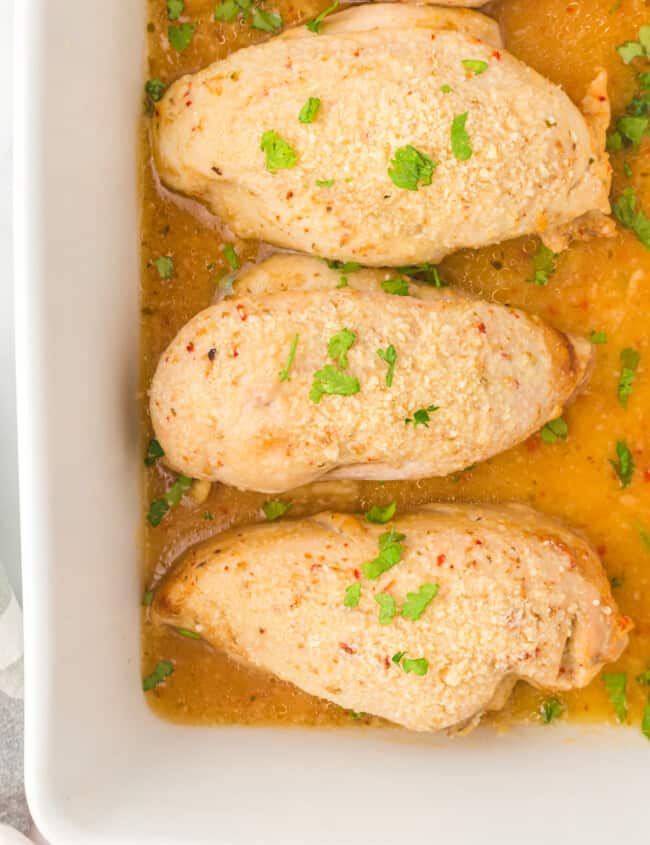 overhead image of baked Italian chicken breasts in a white baking dish