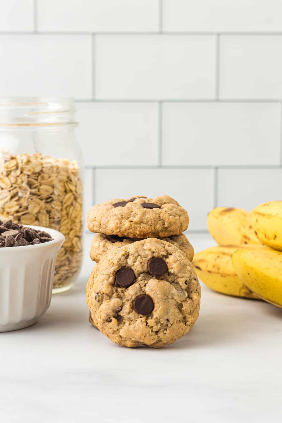 a banana oatmeal cookie leaning on a stack of 3 cookies with bananas and oats.