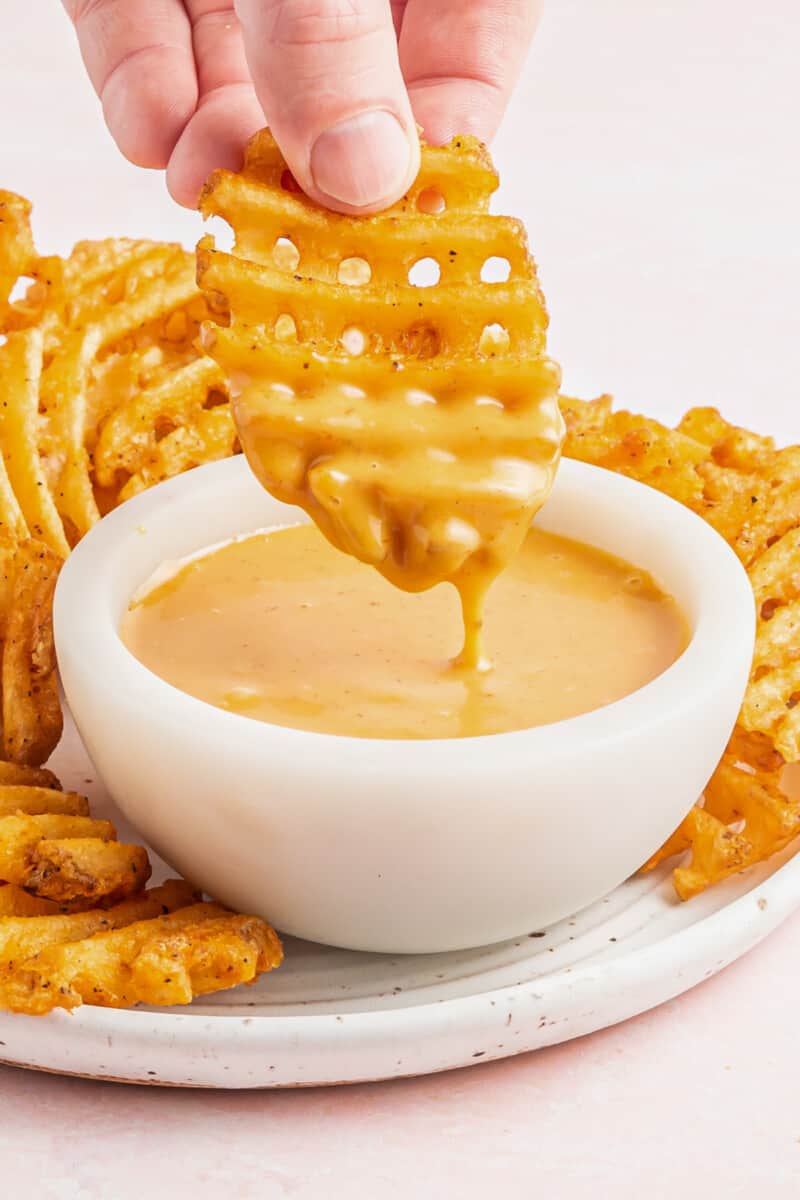 hand dipping a waffle fry into a bowl of chick-fil-a sauce