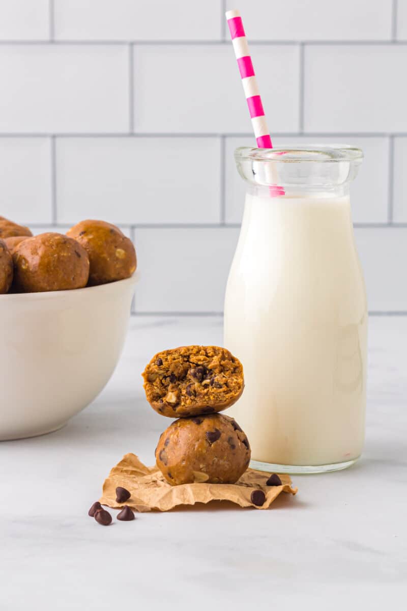 stack of 2 chocolate peanut butter protein balls with a bite taken from the top one with a glass jar of milk